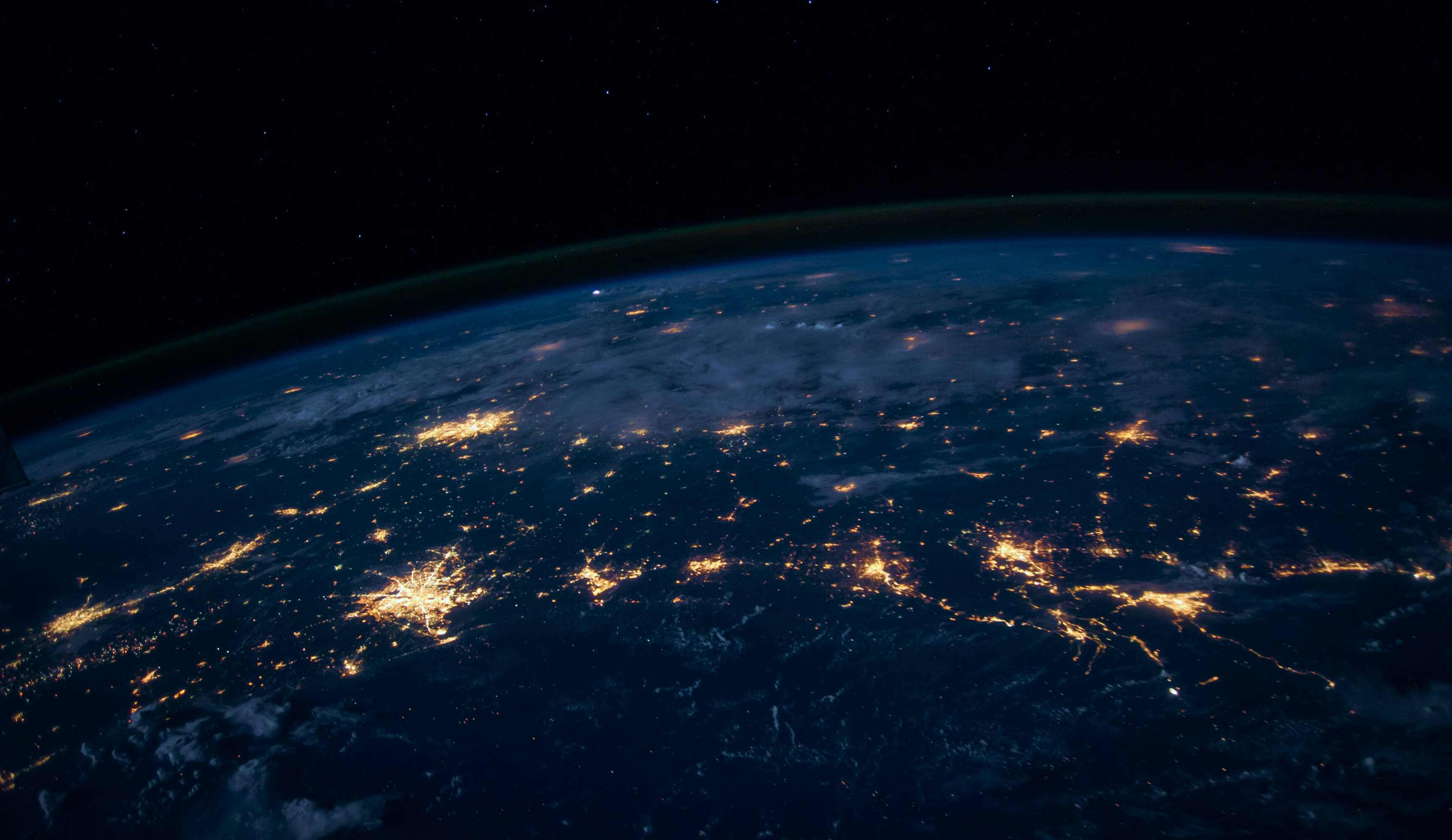 View of Earth at night from space showing city lights and starry sky above the horizon.